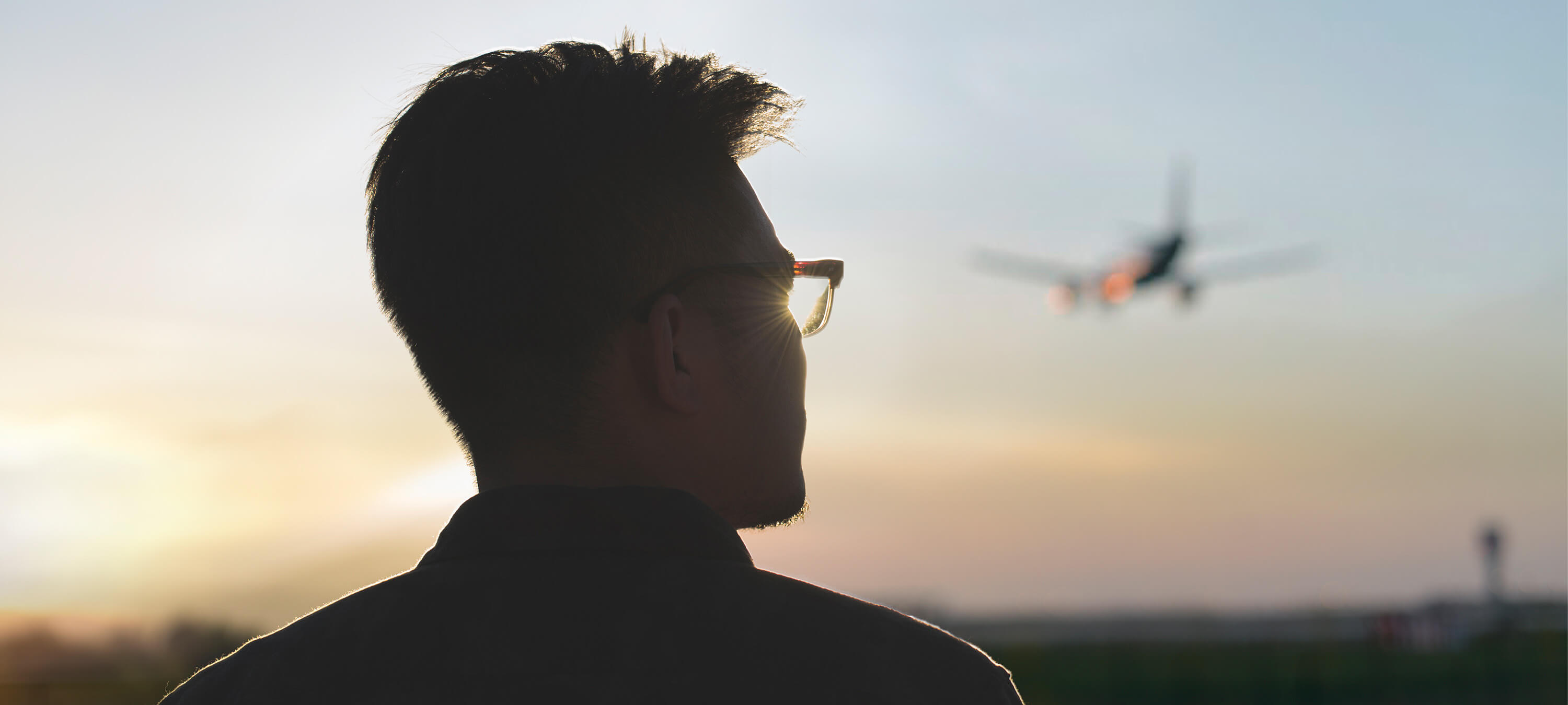 Junger Mann schaut hoffnungsvoll dem Sonnenuntergang entgegen, im Himmel ist ein Flugzeug ist im Hintergrund zu sehen. © Stocksy, Juan Moyano, Zheng Long 