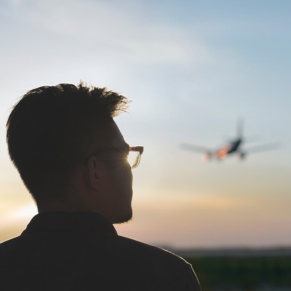 Junger Mann schaut hoffnungsvoll dem Sonnenuntergang entgegen, im Himmel ist ein Flugzeug ist im Hintergrund zu sehen. © Stocksy, Juan Moyano, Zheng Long 