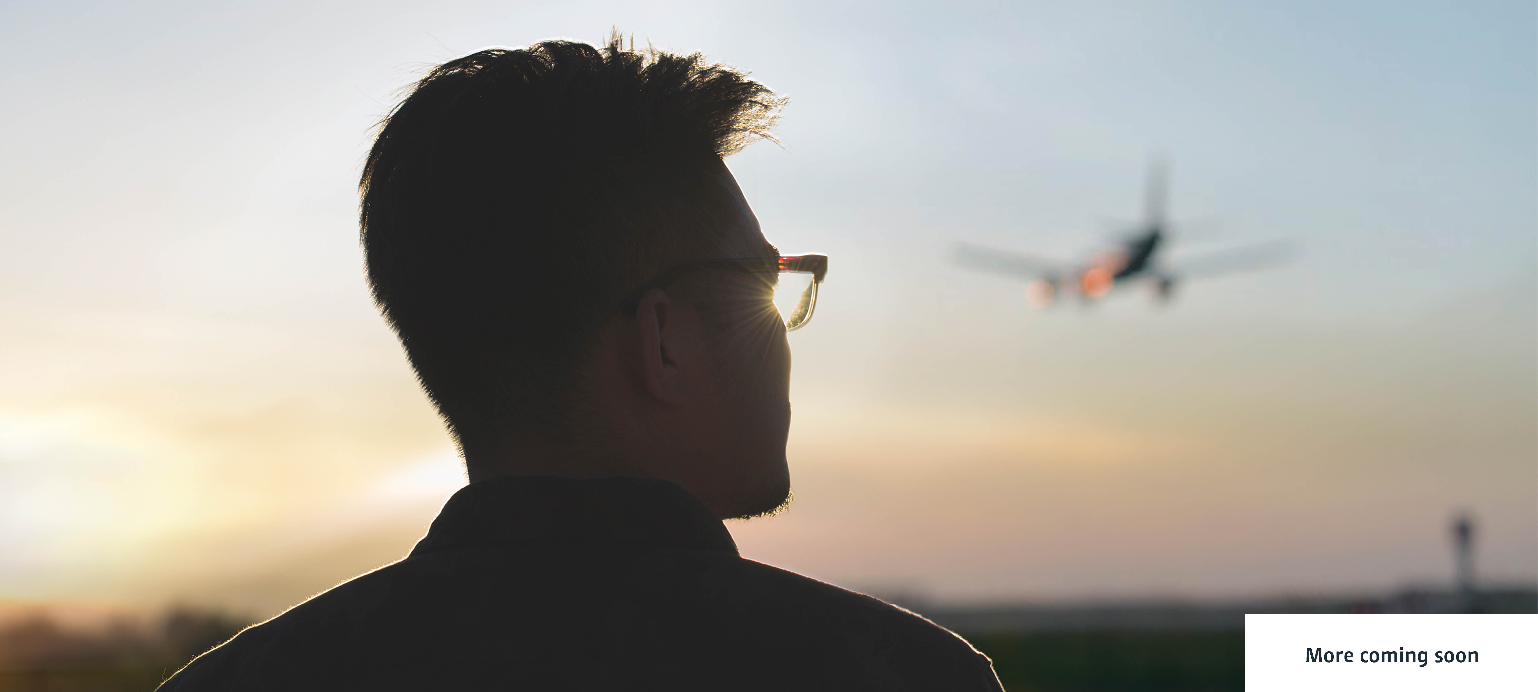 Young man looks hopefully towards the sunset, an aeroplane can be seen in the sky in the background. © Stocksy, Juan Moyano, Zheng Long 